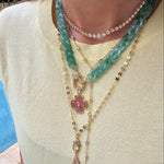 Close-up of a woman wearing layered jewelry, including necklaces, earrings, and bracelets. Her face is not visible, focusing attention on the fine details and textures of each piece. The image also features a zoomed-in view of similar jewelry worn by others, showcasing the versatility of the collection.