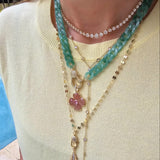 Close-up of a woman wearing layered jewelry, including necklaces, earrings, and bracelets. Her face is not visible, focusing attention on the fine details and textures of each piece. The image also features a zoomed-in view of similar jewelry worn by others, showcasing the versatility of the collection.