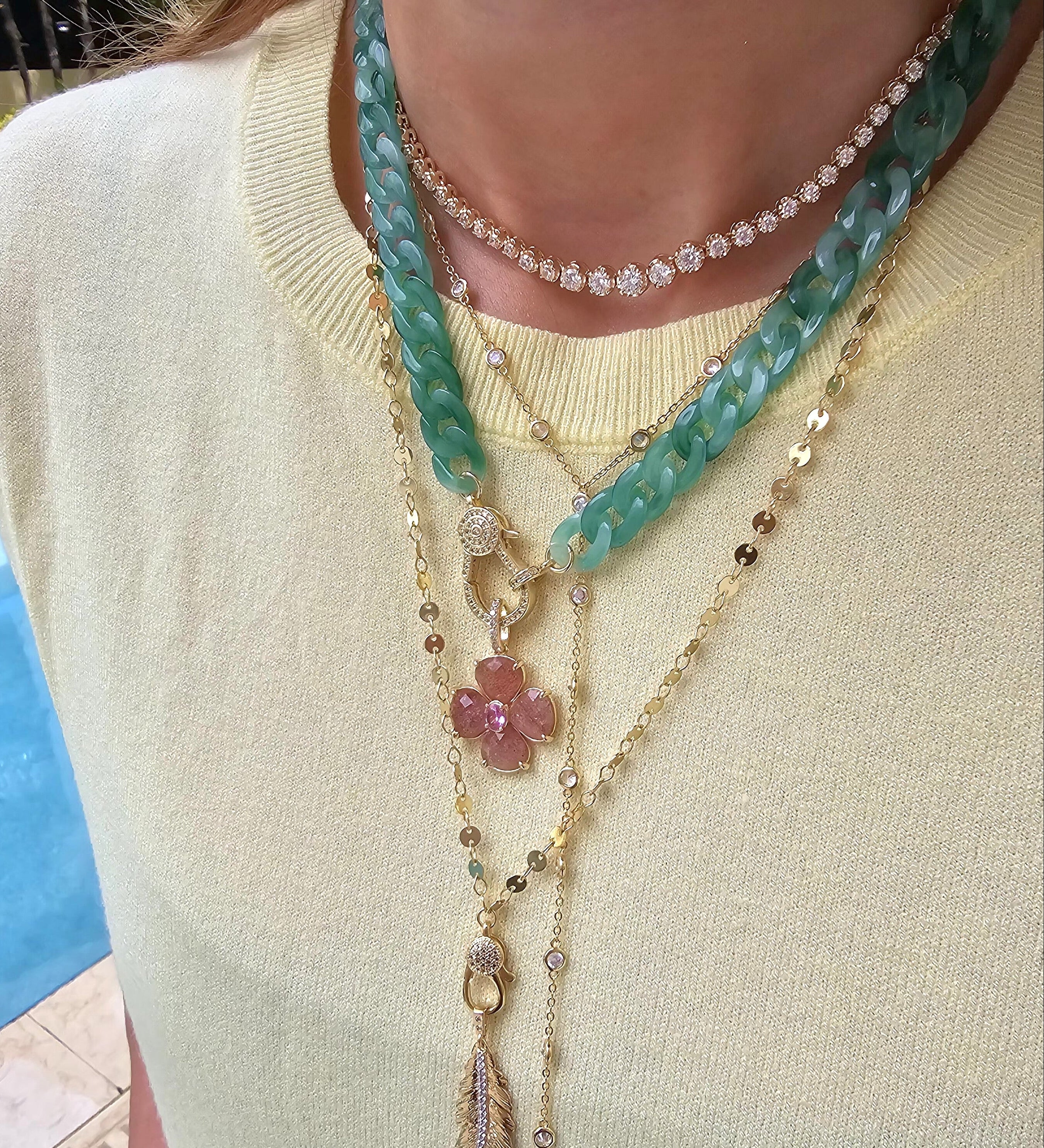 Close-up of a woman wearing layered jewelry, including necklaces, earrings, and bracelets. Her face is not visible, focusing attention on the fine details and textures of each piece. The image also features a zoomed-in view of similar jewelry worn by others, showcasing the versatility of the collection.