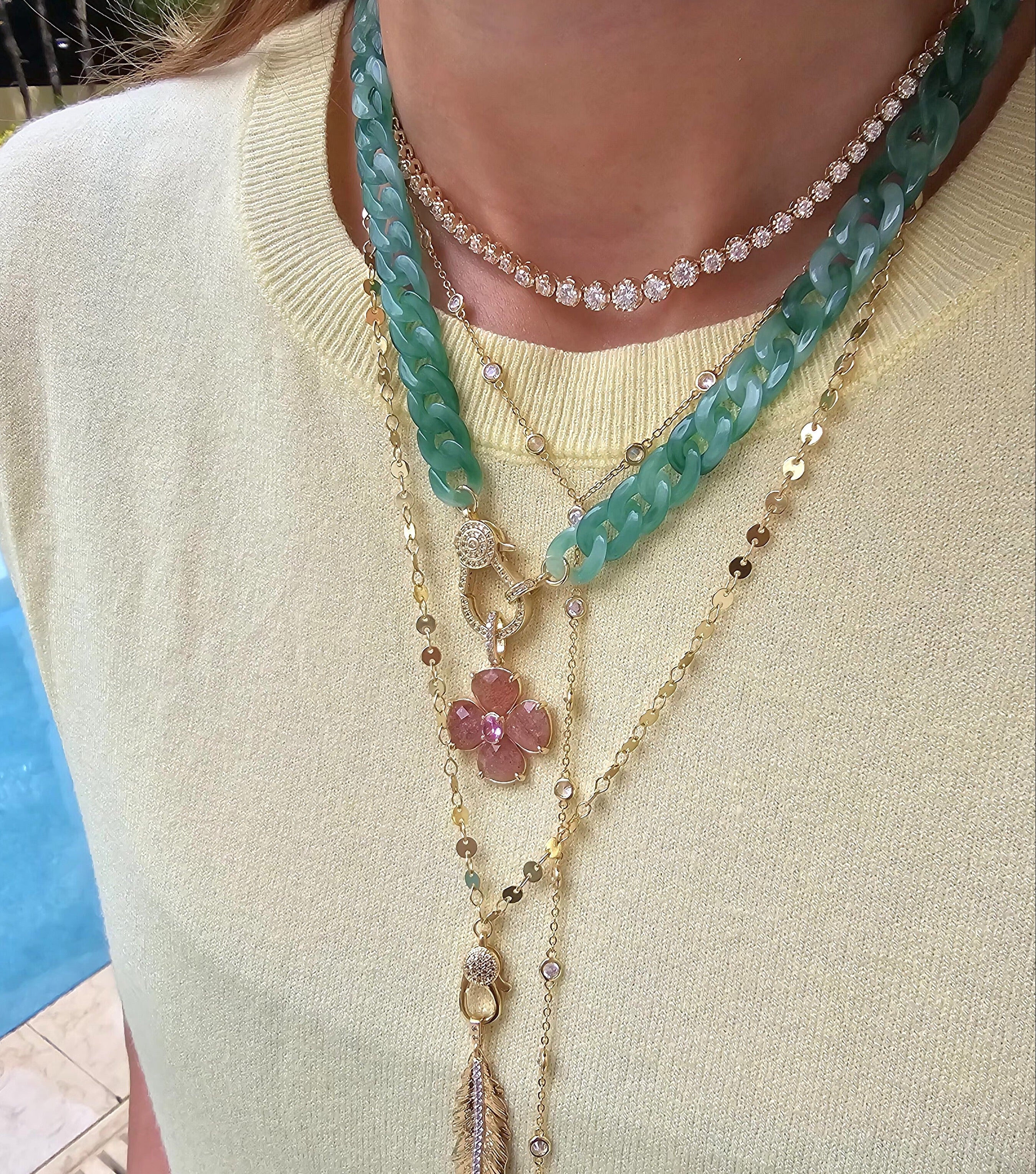 Close-up of a woman wearing layered jewelry, including necklaces, earrings, and bracelets. Her face is not visible, focusing attention on the fine details and textures of each piece. The image also features a zoomed-in view of similar jewelry worn by others, showcasing the versatility of the collection.